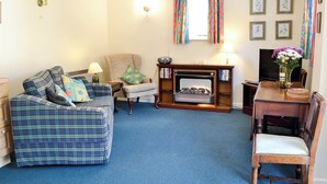 A living room with a plaid sofa, a chair, a fireplace, a television, and a dining table. - Pig Sty Cottage - E1867 (West Milton)