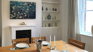 Ein Esszimmer mit Holztisch, gedeckt für vier Personen, Kamin und Regalen mit dekorativen Flaschen.