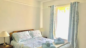 Ein Schlafzimmer mit einem Bett, zwei Nachttischlampen, einem Nachttisch und einem Fenster mit Vorhängen.
