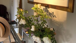 Ein Zimmer mit einer Glastrennwand, einer weißen Vase mit weißen Blumen, einem Holzstuhl und einem Bild an der Wand.