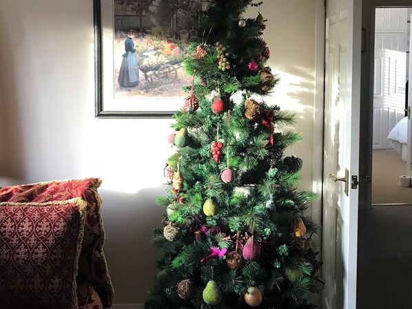 Un árbol de Navidad con adornos varios, un cuadro enmarcado en la pared y una puerta que da a otra habitación.