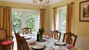 Ein Esszimmer mit Tisch für vier Personen, Stühlen, einer Chandelieber und großen Fenstern mit Vorhängen.