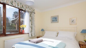 Een slaapkamer met een bed, twee nachtkastjes, een raam met gordijnen, een radiator en een muur met twee ingelijste foto’s.