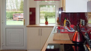 A modern kitchen with a black induction cooktop, white cabinets, and a red window blind. - Blaeberry Cottage - 28061 (Near Lockerbie)