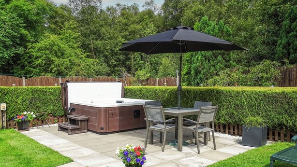 A backyard with a hot tub, patio table, chairs, and an umbrella. - Blaeberry Cottage - 28061 (Near Lockerbie)