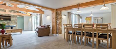 A spacious living area with a sofa, dining table, and chairs, wooden beams, and a fireplace.