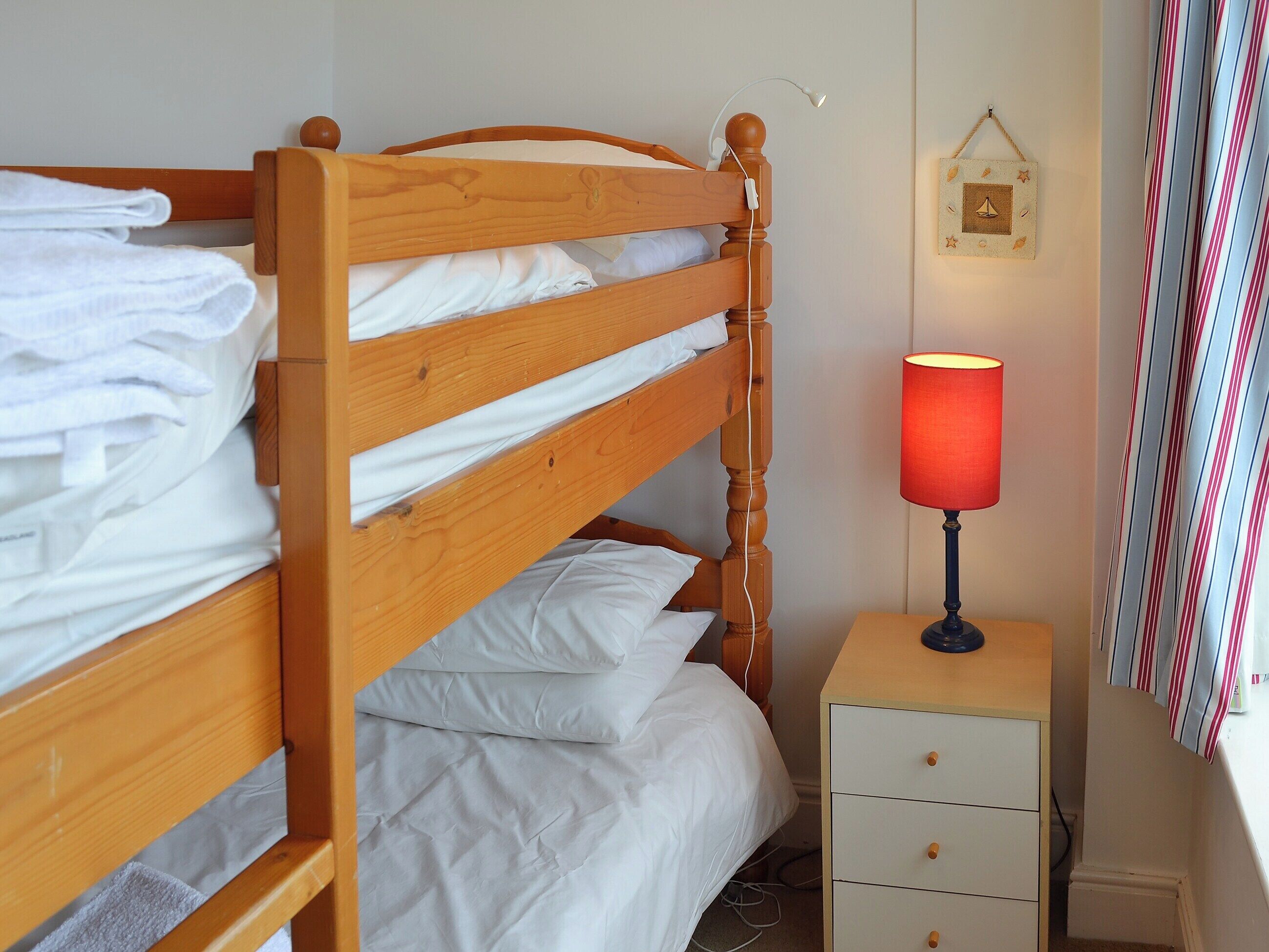 Un lit superposé avec une literie blanche, une table de chevet avec une lampe et un rideau à rayures.