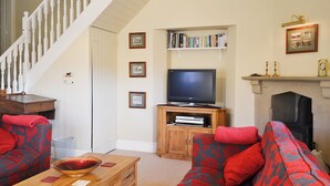 A living room with a staircase, a television on a wooden stand, a fireplace, and a bookshelf with books.