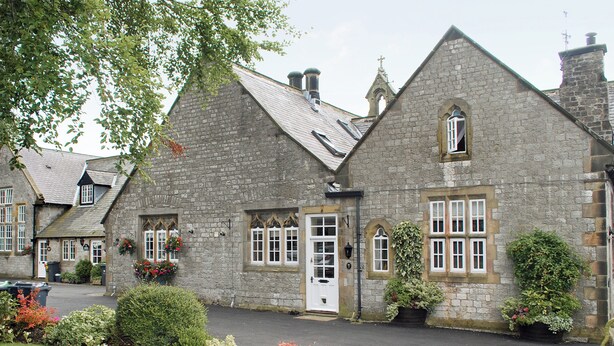 A stone building with a traditional architectural style, featuring a central entrance, multiple windows, and a small bell tower.