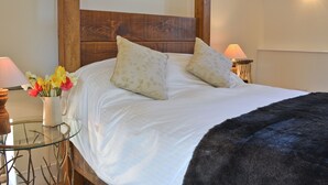 Una cama bien hecha con dos almohadas, una mesita de noche con un jarrón de flores y una lámpara.