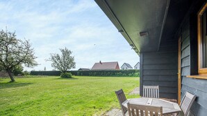 Eine Terrasse mit Tisch und Stühlen, eine Rasenfläche und ein Gebäude mit dunkler Fassade.