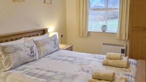 Una cama bien hecha con una colcha de motivos florales, dos almohadas con diseños de ciervos y dos toallas enrolladas sobre la cama.