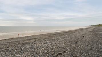 A pebbled beach with a clear view of the sea and distant hills.