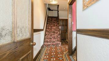 A hallway with a patterned floor, a wooden door, a staircase with a patterned carpet, and a hanging light fixture.