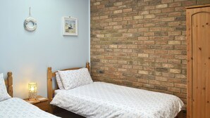 Un dormitorio con dos camas individuales, un armario de madera, una pared de ladrillo y un cuadro en la pared.