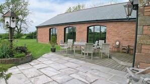 A patio with stone flooring, outdoor seating, and a brick building with large windows. - 6 bedroom accommodation in Arkleby, near Cockermouth (Arkleby, near Cockermouth)