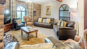 A living room with leather sofas, a wooden coffee table, a television, and a stone wall. - 6 bedroom accommodation in Arkleby, near Cockermouth (Arkleby, near Cockermouth)