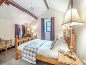 Un dormitorio con cama de madera, una mesita de noche con lámpara, un aparador con espejo y una ventana con cortinas.