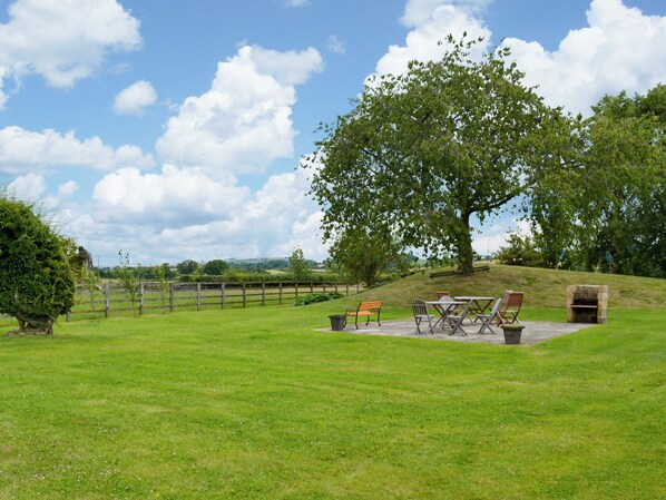 A grassy outdoor area with a large tree, a stone fireplace, and outdoor seating.