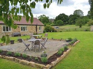 A stone house with a red-tiled roof, a patio with wooden furniture, and a well-maintained garden.