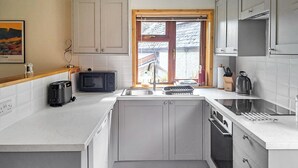 Cocina compacta con muebles blancos, horno integrado, lavamanos y ventana con vista al exterior.