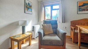 Un salón acogedor con suelo de madera, un sillón azul, una mesa de madera, una lámpara y un radiador.