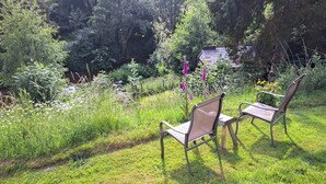 Dos sillas sobre un césped con un jardín y árboles al fondo.
