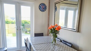 A dining area with a table covered in a polka dot tablecloth, a vase with orange flowers, and a clock on the wall. - 3 bedroom accommodation in Padstow (Padstow)
