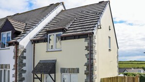 A two-story house with a sloped roof, stone cladding, and a wooden fence. - 3 bedroom accommodation in Padstow (Padstow)