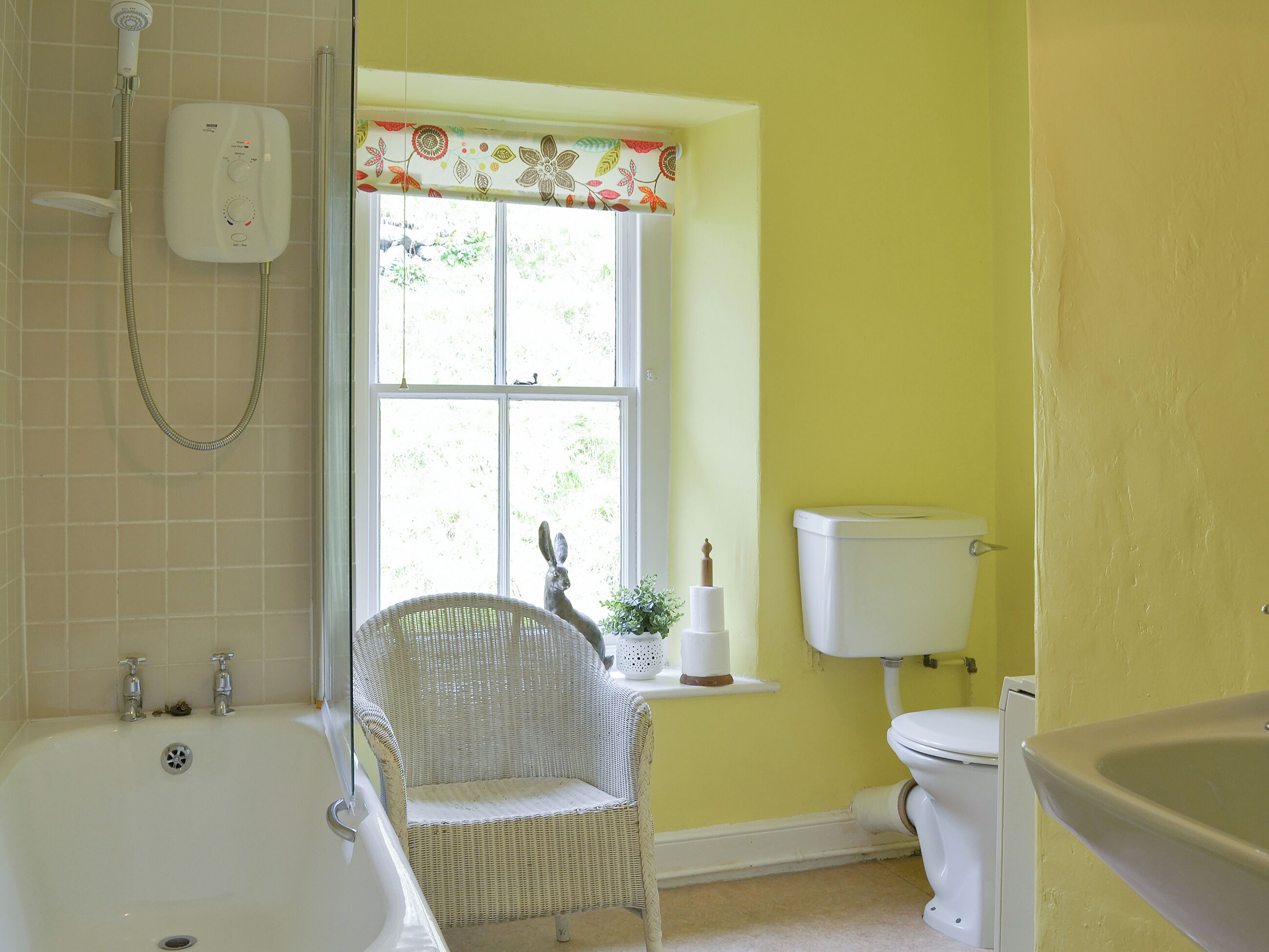 A bathroom with a bathtub, a toilet, and a window with a decorative valance.
