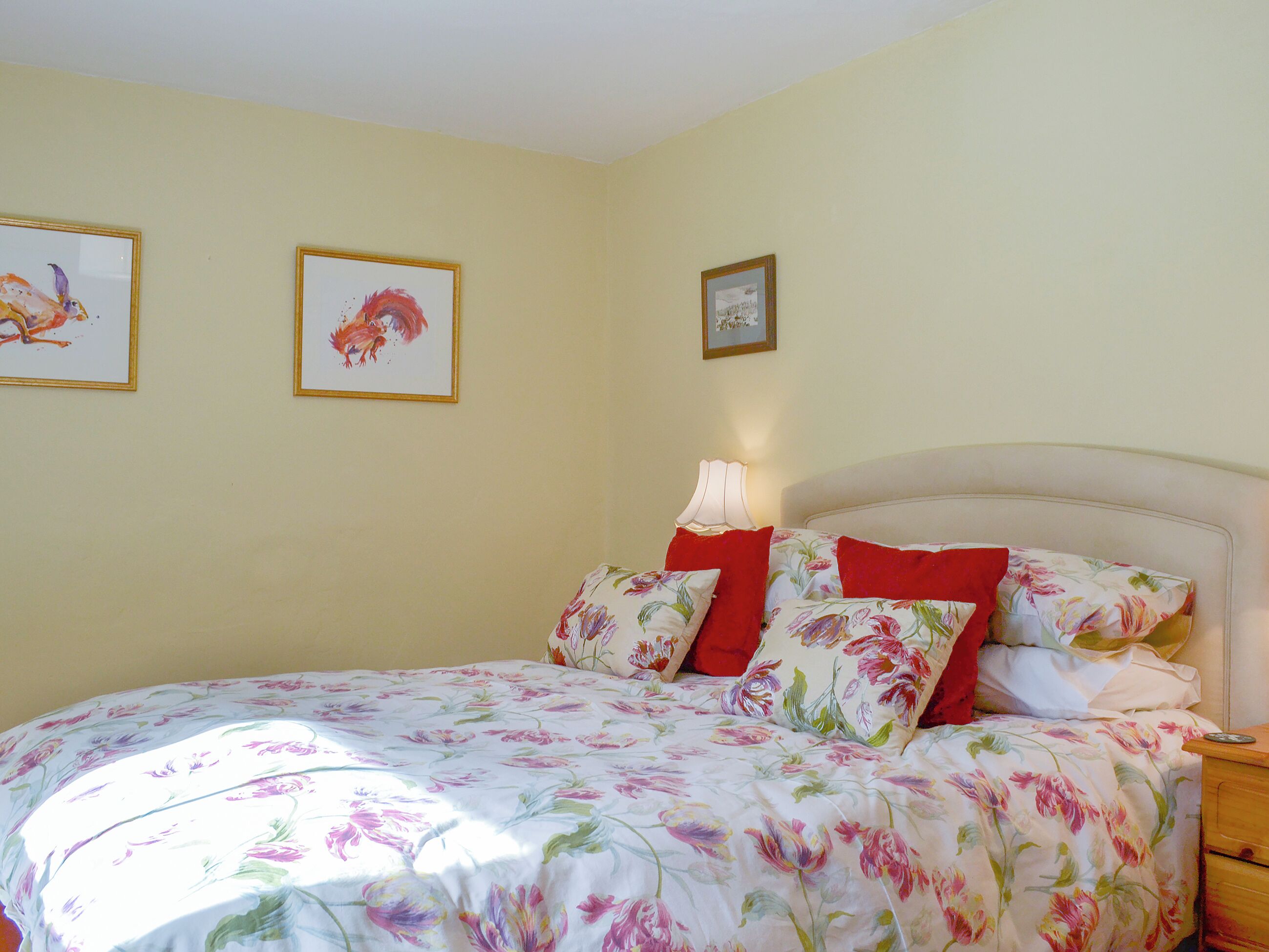 Un dormitorio con una colcha estampada con motivos florales, un cabecero y tres cuadros en la pared.
