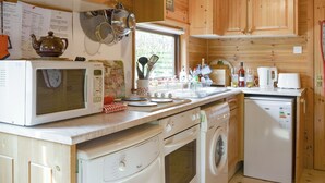 Una cocina compacta con armarios de madera, microondas, lavadora y pileta.
