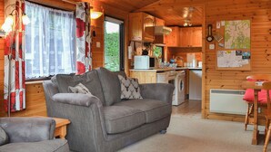 Un interior de cabaña acogedor con un sofá gris, una mesa de comedor de madera y una zona de cocina.