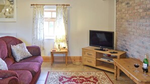 Uma sala de estar acolhedora com um sofá, uma televisão, uma mesa de madeira com uma garrafa e copos, e um tapete estampado.