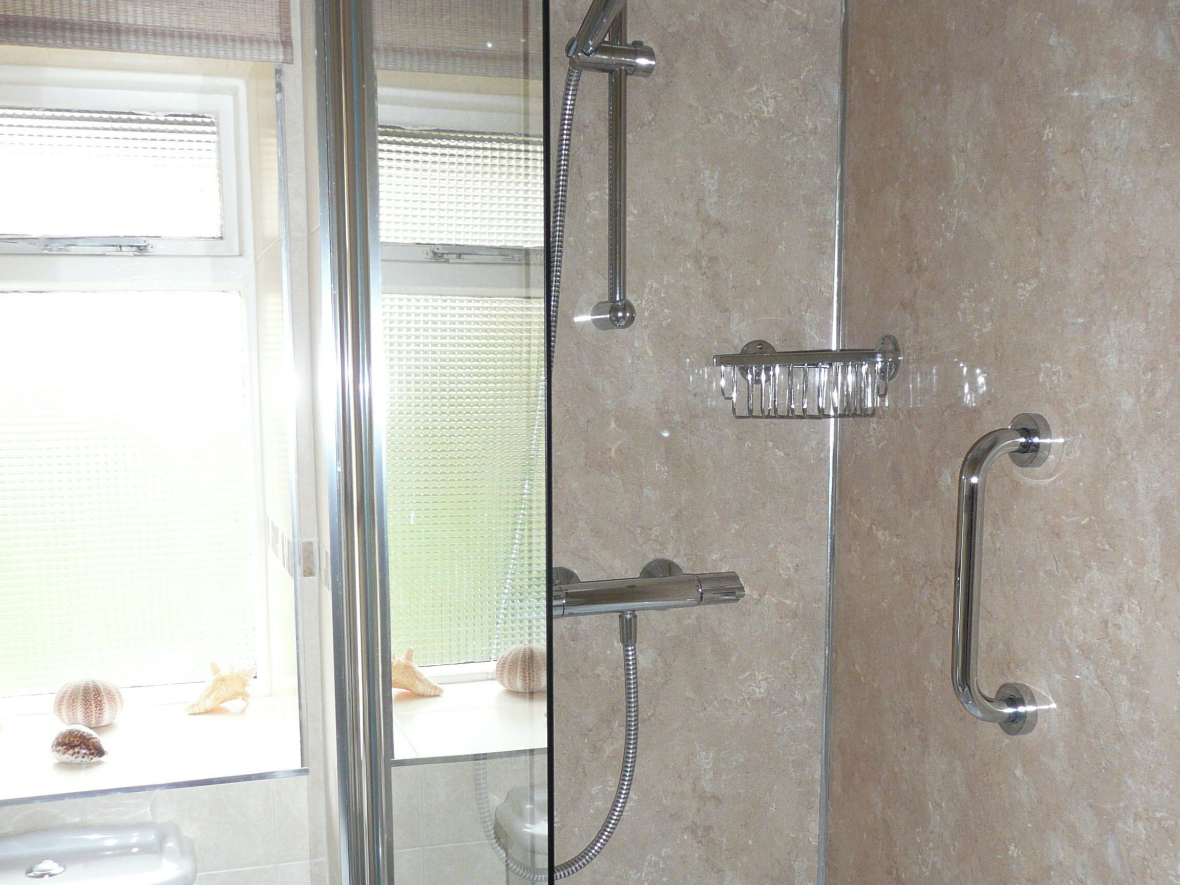 Een douche met een handdouche, een doucheaanslag voor de hand en een muurbevestigde kraan.