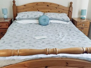 A bed with a patterned bedspread, two pillows, a bedside table with a lamp, and a nightstand with a lamp.