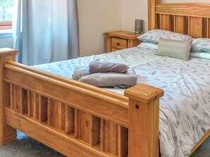 Una cama de madera con una colcha y almohadas estampadas, una mesita de noche con una lámpara y una ventana con cortinas.