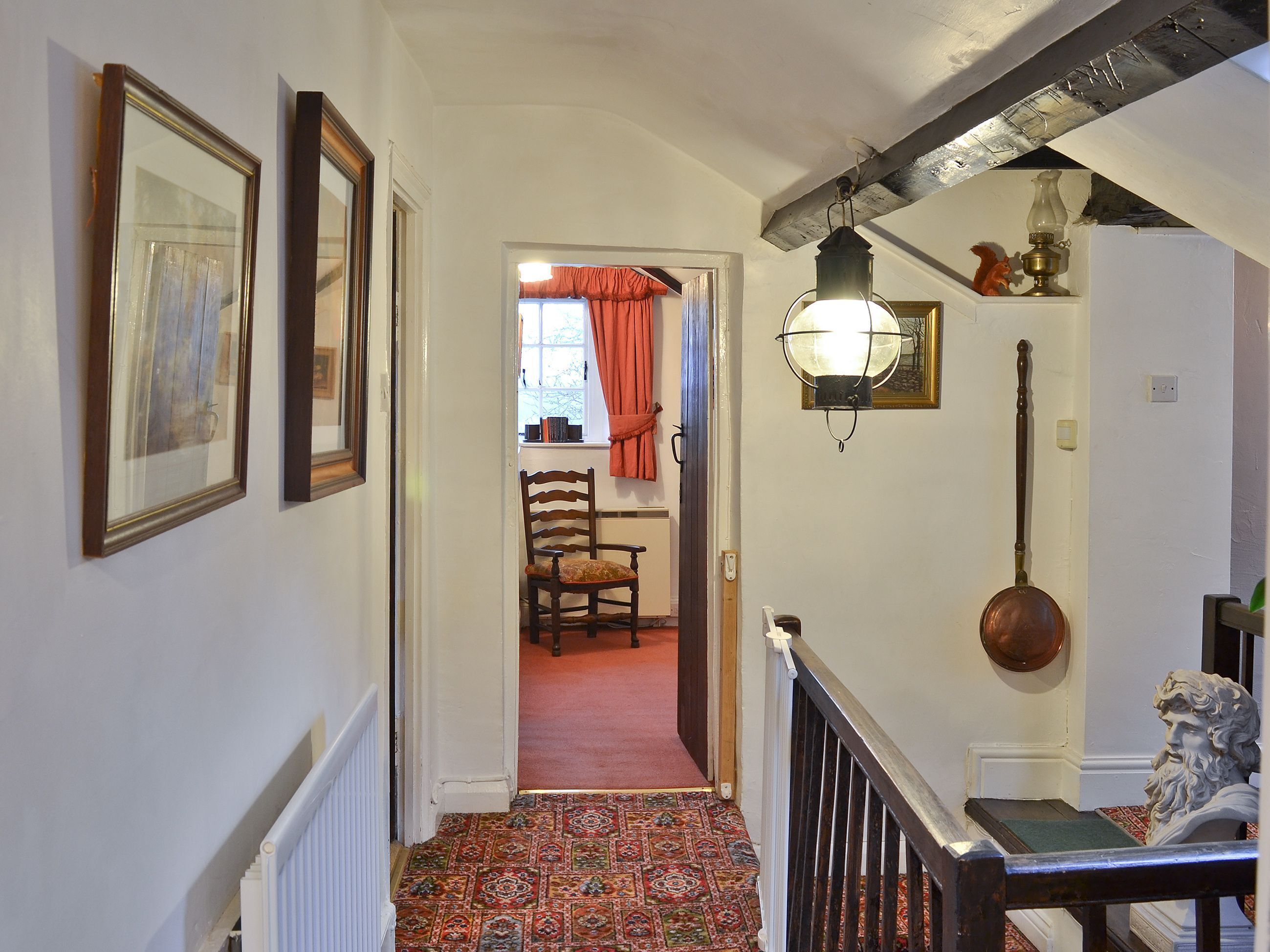 A hallway with a patterned carpet, a wooden chair, and a staircase with a black railing.