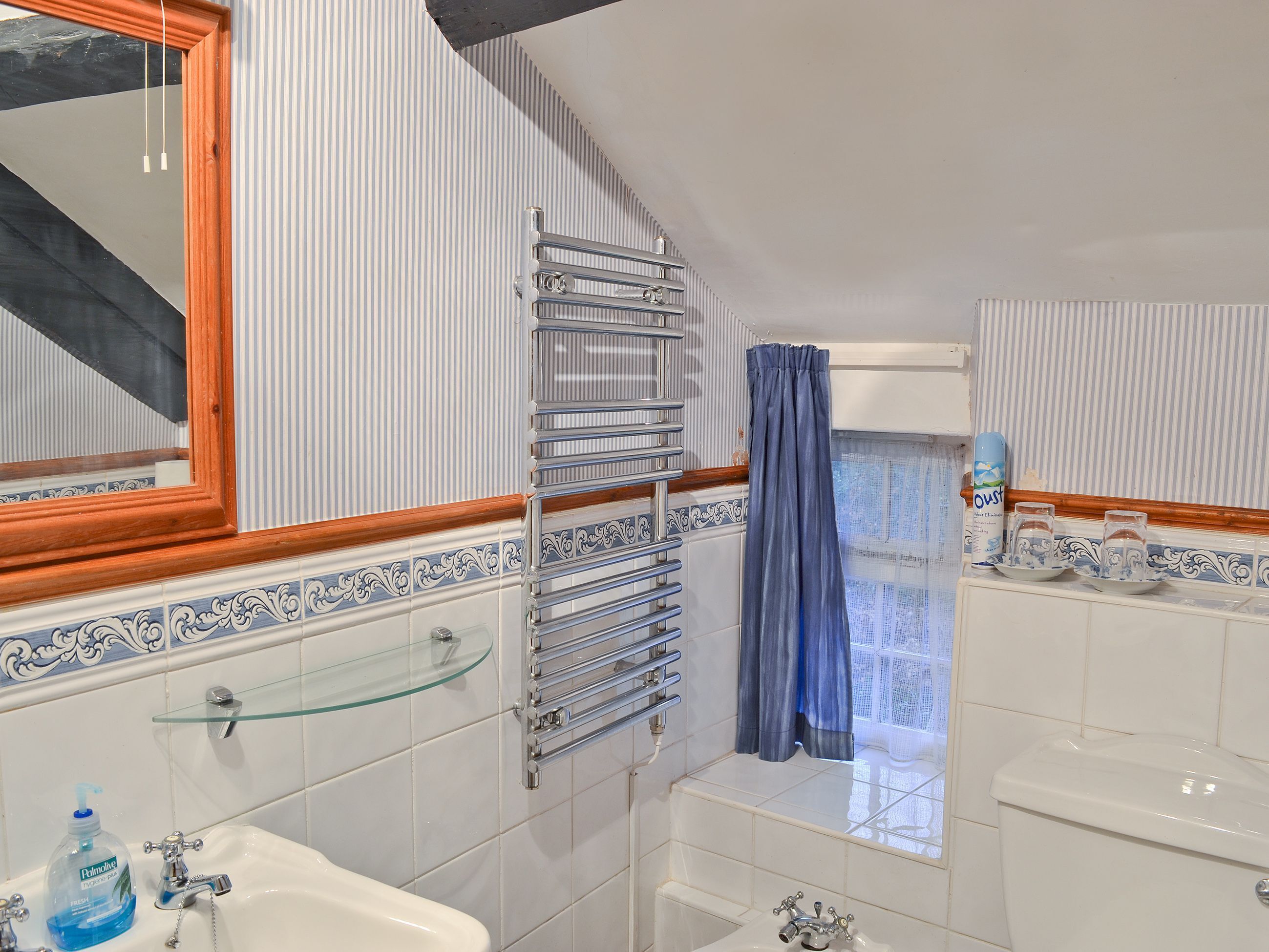 A bathroom with a glass shelf, a towel rack, a toilet, and a window with a curtain.