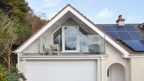 A single-story house with a garage, a balcony with glass railings, and solar panels on the roof. - The lounge is a room with a view. (Heybrook Bay, near Plymouth)