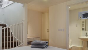 A bedroom with a bed, a bedside table, a nightstand, a wardrobe, and a bathroom with a sink and mirror. - The lounge is a room with a view. (Heybrook Bay, near Plymouth)