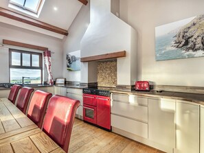 Una cocina con una isla grande, un horno rojo y vista al mar a través de una ventana.