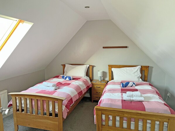 A room with two wooden beds, each with a pillow and a bedside table with a lamp.