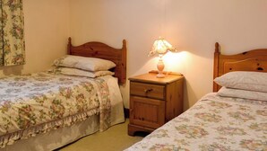 Ein Schlafzimmer mit zwei Einzelbetten, jeweils mit floralem Bettbezug, einem Nachttisch mit Lampe und einem Holzkopfende.