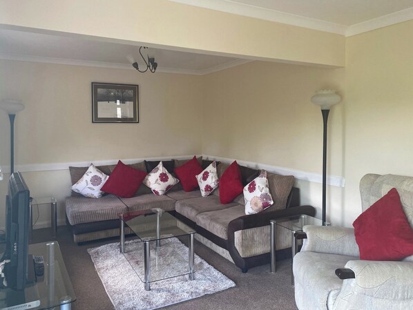 A living room with a sectional sofa, a glass coffee table, and a television.
