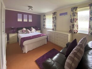 A bedroom with a bed, nightstands, a dresser, a window with curtains, and a purple rug.