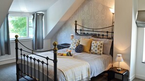 A bedroom with a sloped ceiling, a bed with patterned pillows, a bedside lamp, and a window with curtains. - 3 bedroom accommodation in Llangoed, near Beaumaris (Llangoed, near Beaumaris)