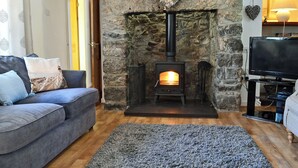 A cozy living room with a stone fireplace, a grey sofa, and a television. - 3 bedroom accommodation in Llangoed, near Beaumaris (Llangoed, near Beaumaris)