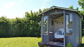 A small, single-room shed with a bed, a window, and a door. - 3 bedroom accommodation in Llangoed, near Beaumaris (Llangoed, near Beaumaris)