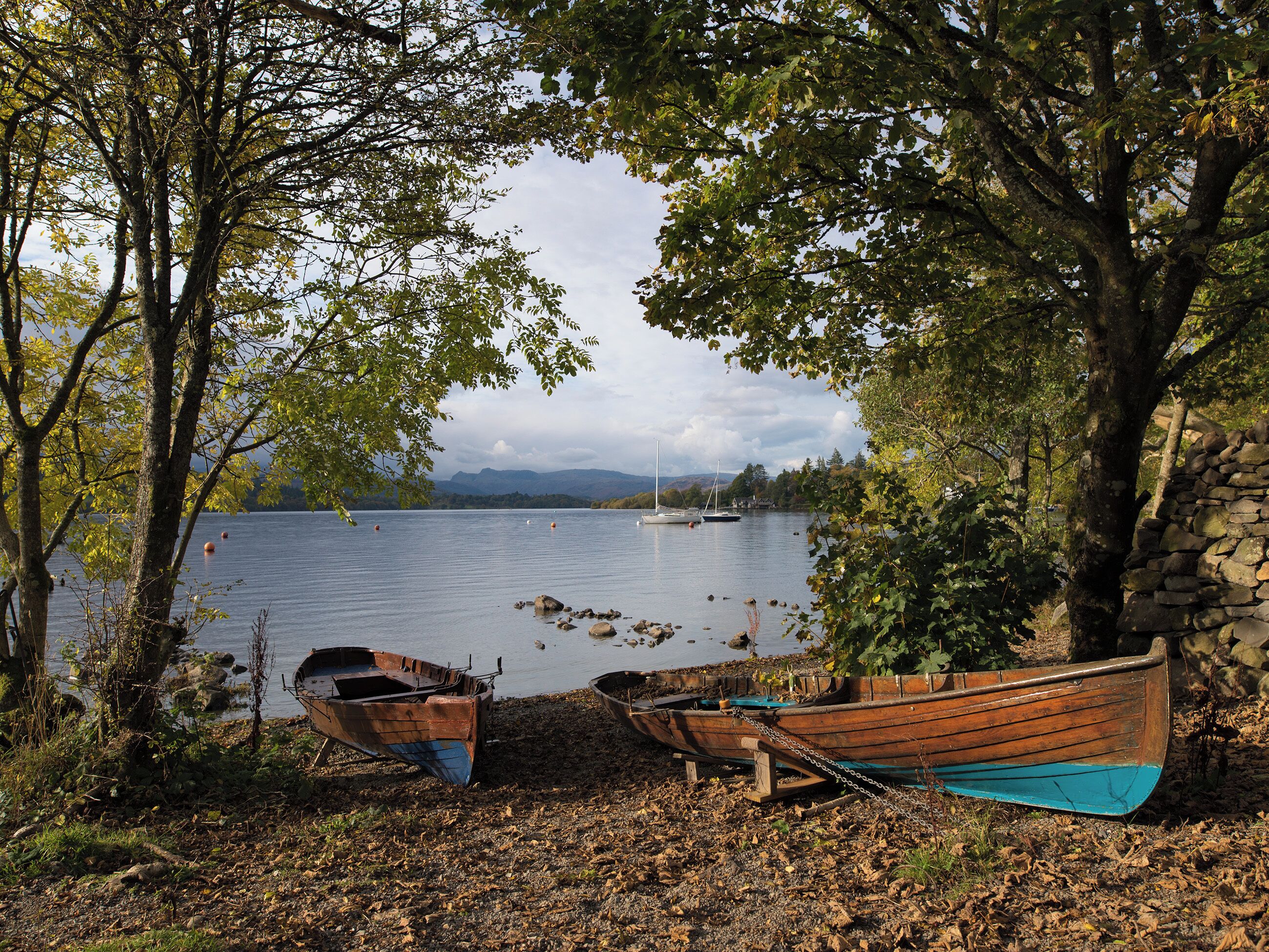 A lakeside scene with boats tied to a tree and a stone wall.
